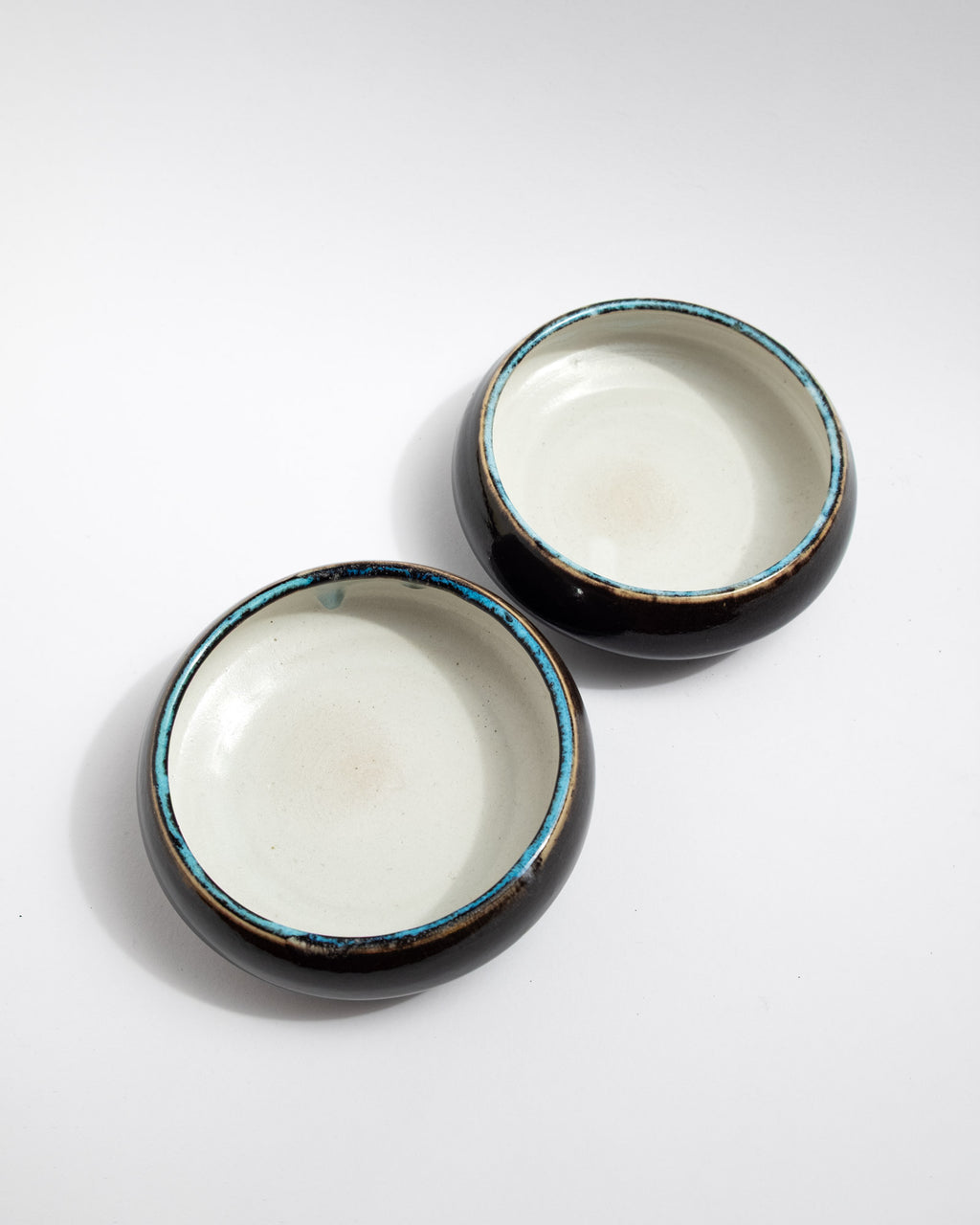 Small handmade bowl with white interior, dark exterior, and turquoise-rim detail
