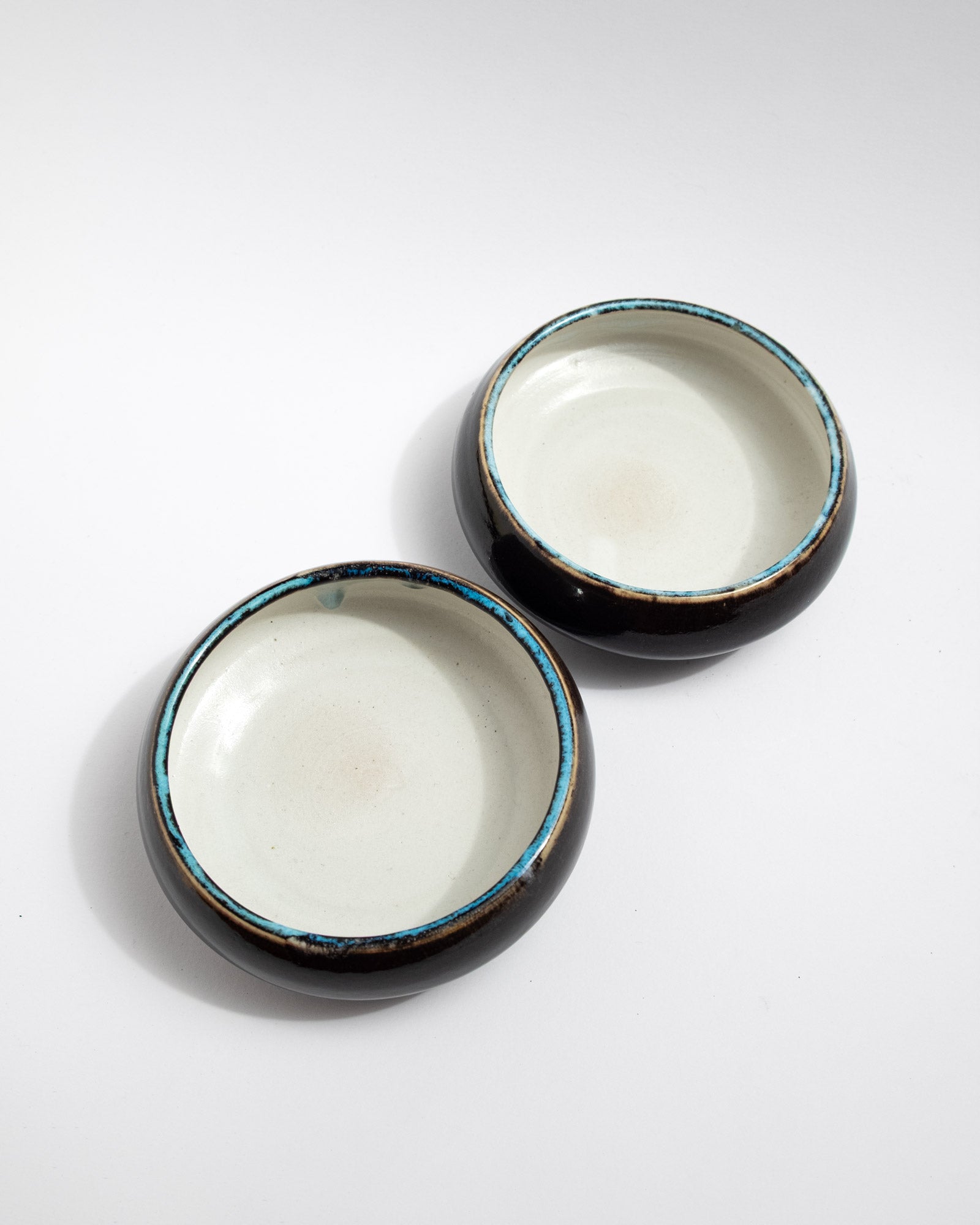 Small handmade bowl with white interior, dark exterior, and turquoise-rim detail