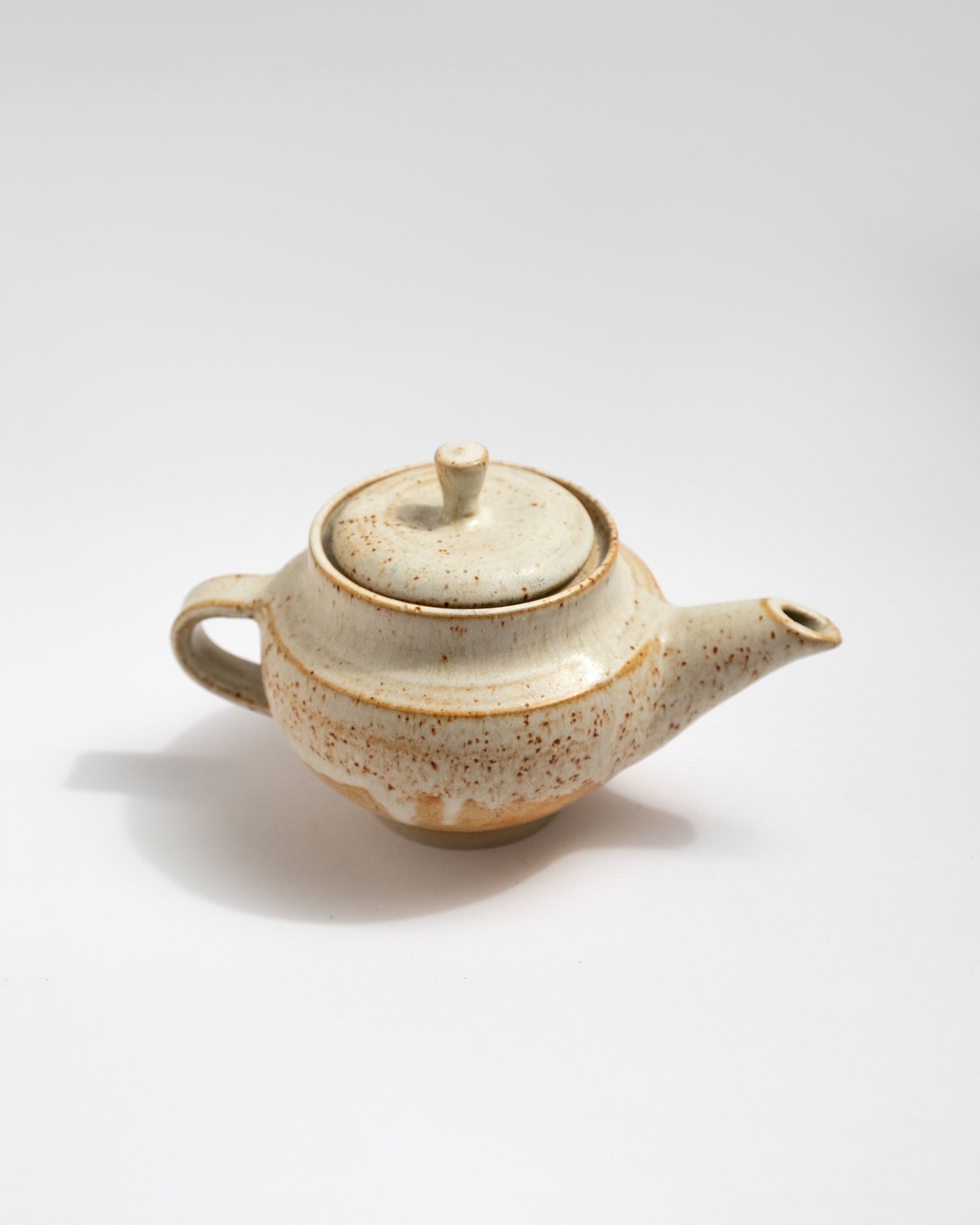 Ceramic handmade teapot with speckled pattern on a white background