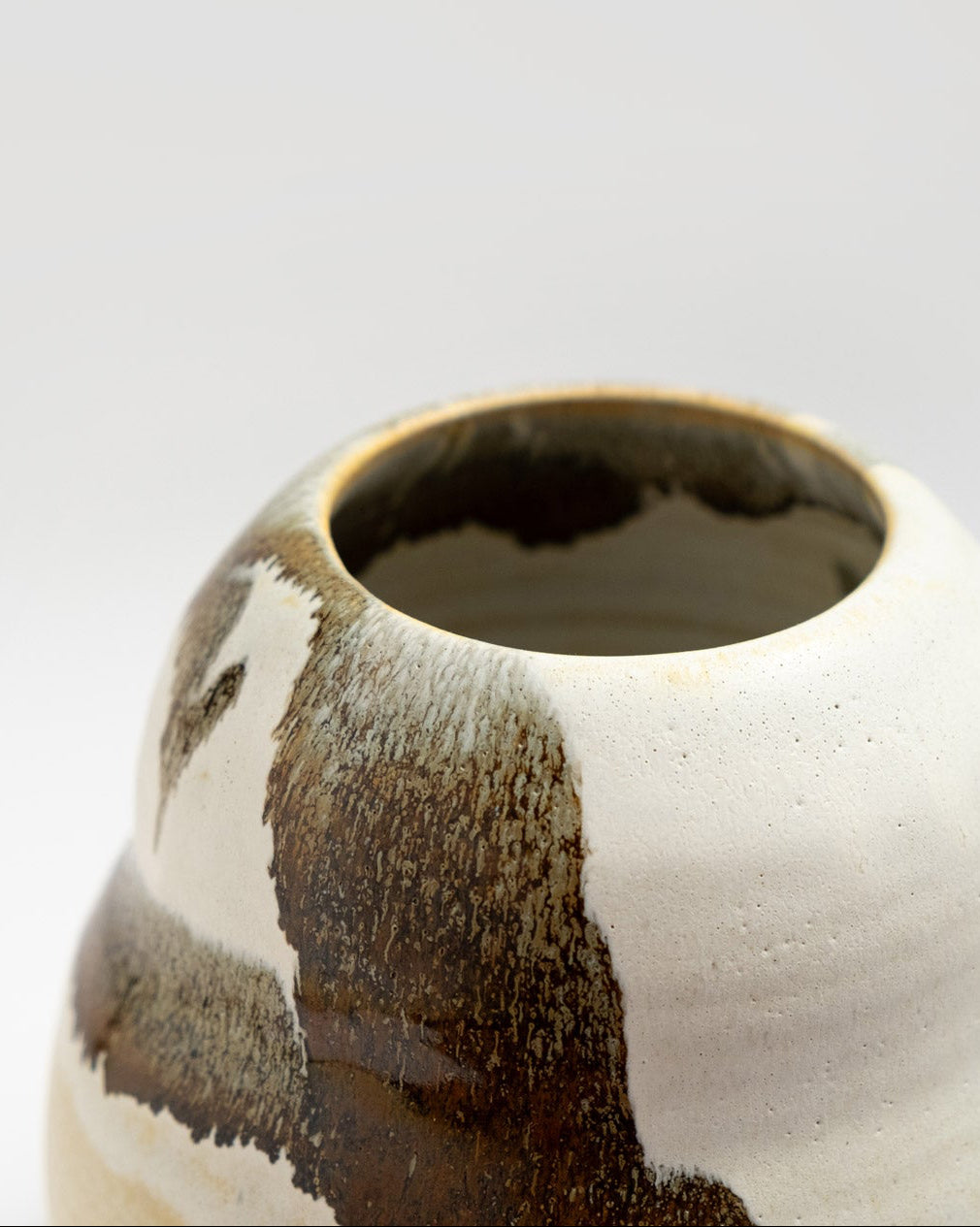 Close-up of a ceramic vase with brown and white glaze on a light gray background