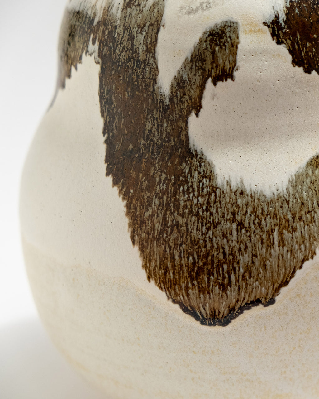 Close-up of a ceramic vase with brown and white glaze on a white background
