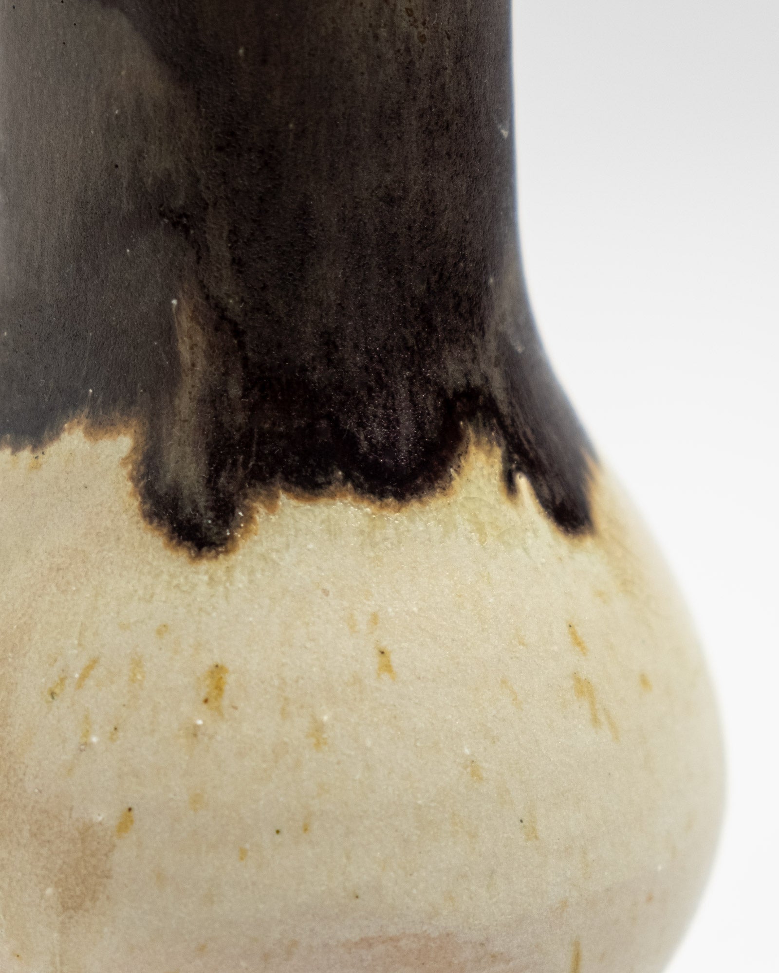 Close-up of a ceramic vase with black and beige glaze on a white background