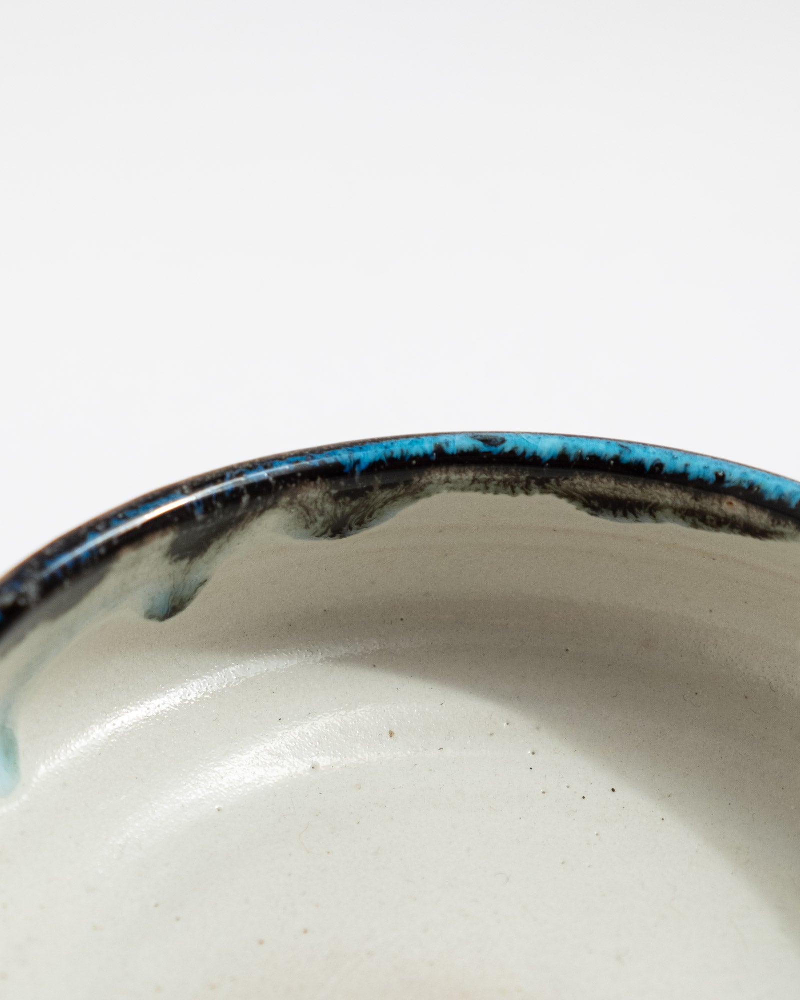 Small handmade bowl with white interior, dark exterior, and turquoise-rim detail