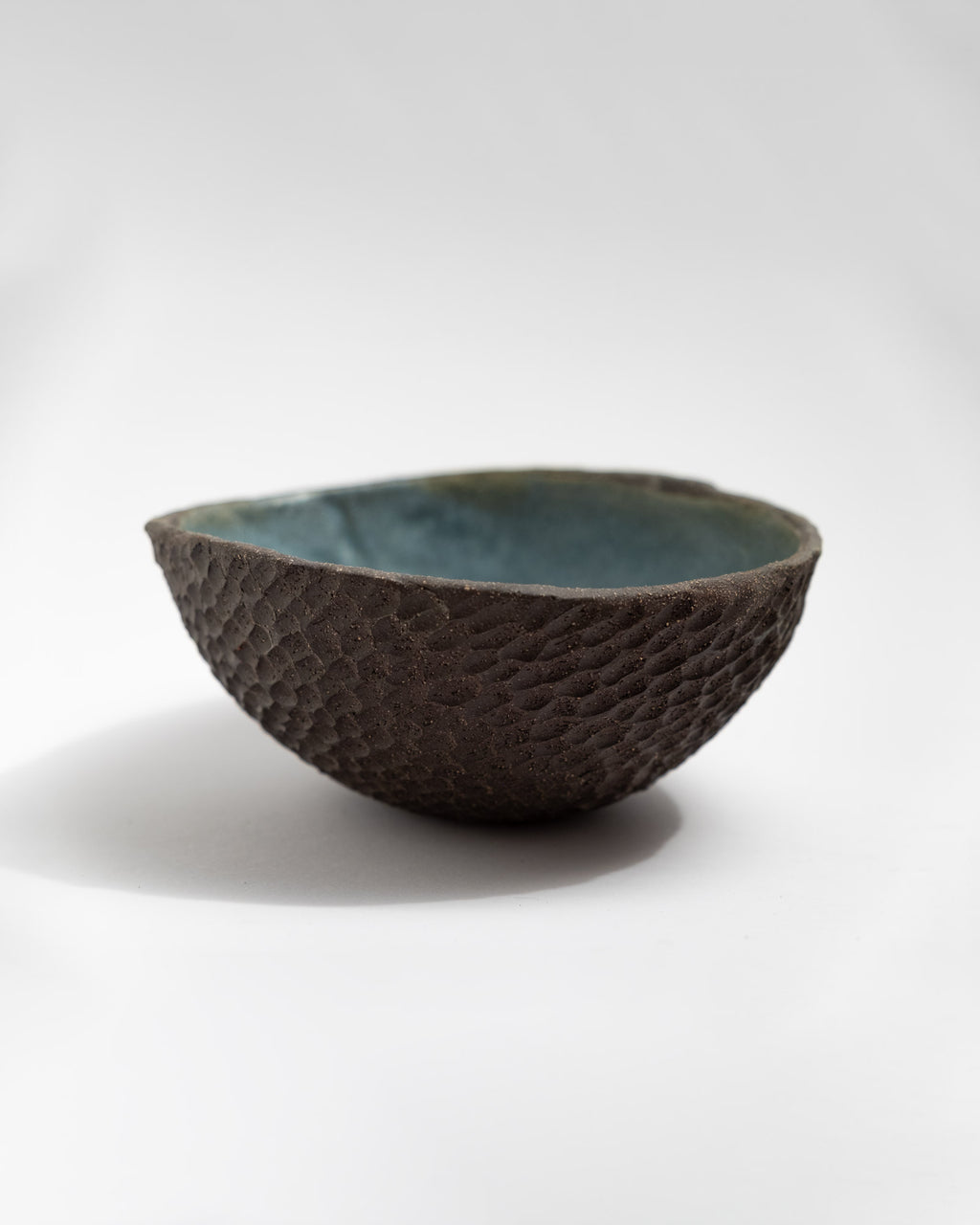 Hand-textured black clay bowl with scale-like surface and blue glazed interior