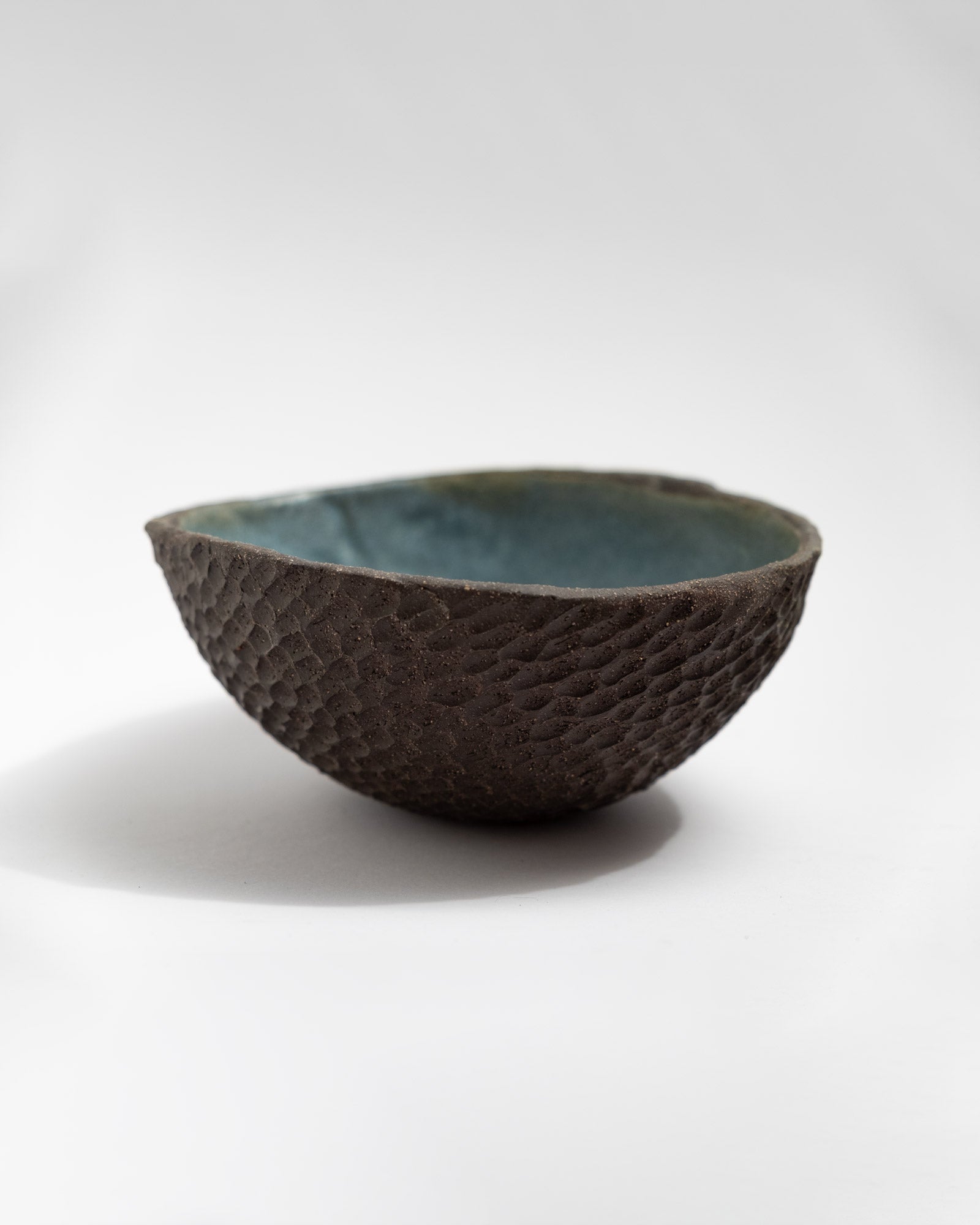 Hand-textured black clay bowl with scale-like surface and blue glazed interior