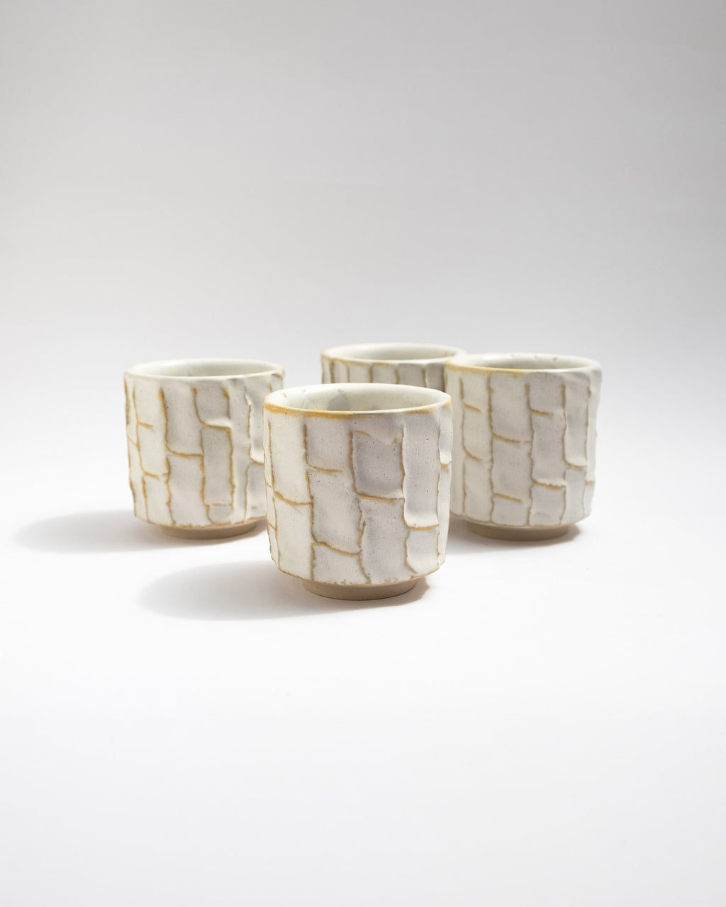 Handmade white ceramic cups with a kurinuki pattern on a white background