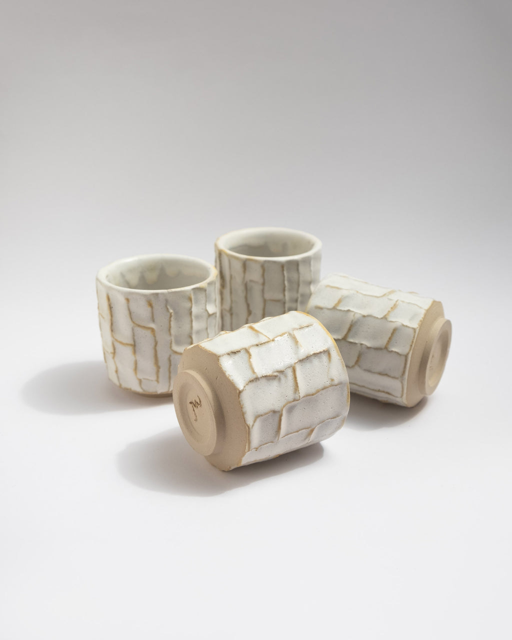 Set of four ceramic tea cups with handmade patterns on a light gray background