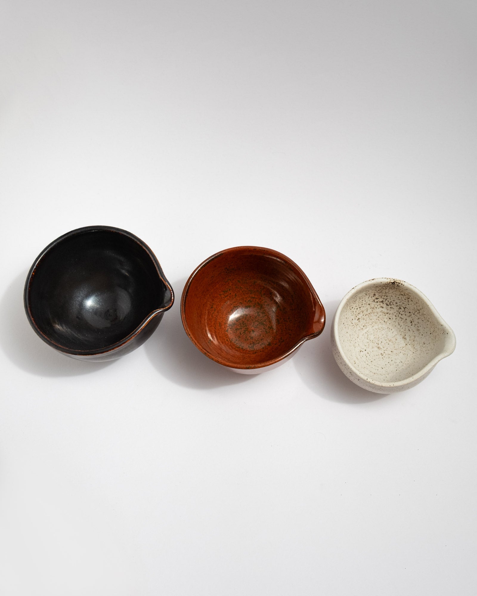 Set of three small handmade stoneware pouring bowls in black, rust-red, and speckled white glazes