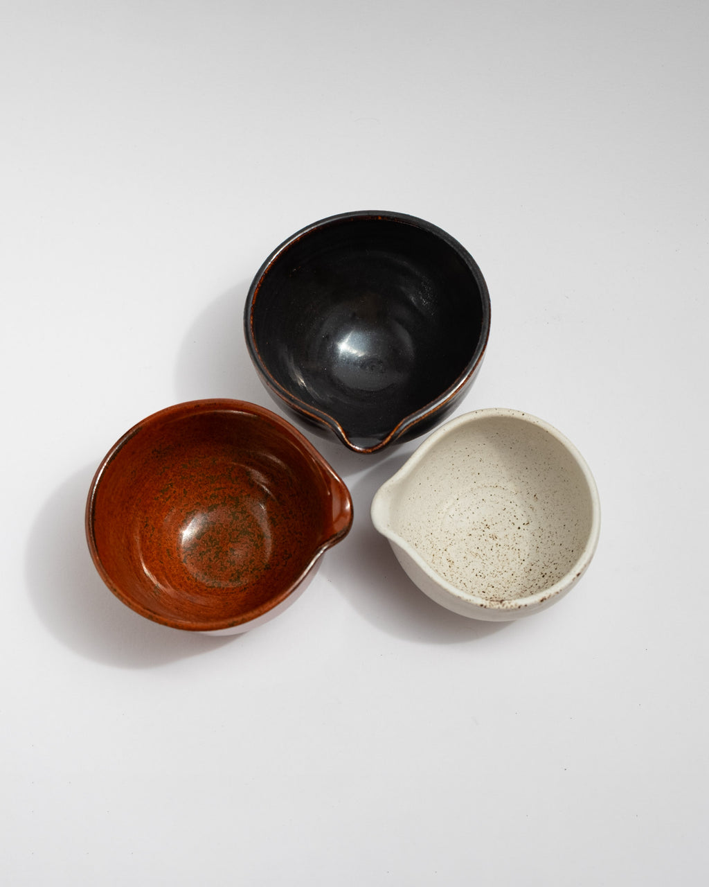 Set of three small handmade stoneware pouring bowls in black, rust-red, and speckled white glazes