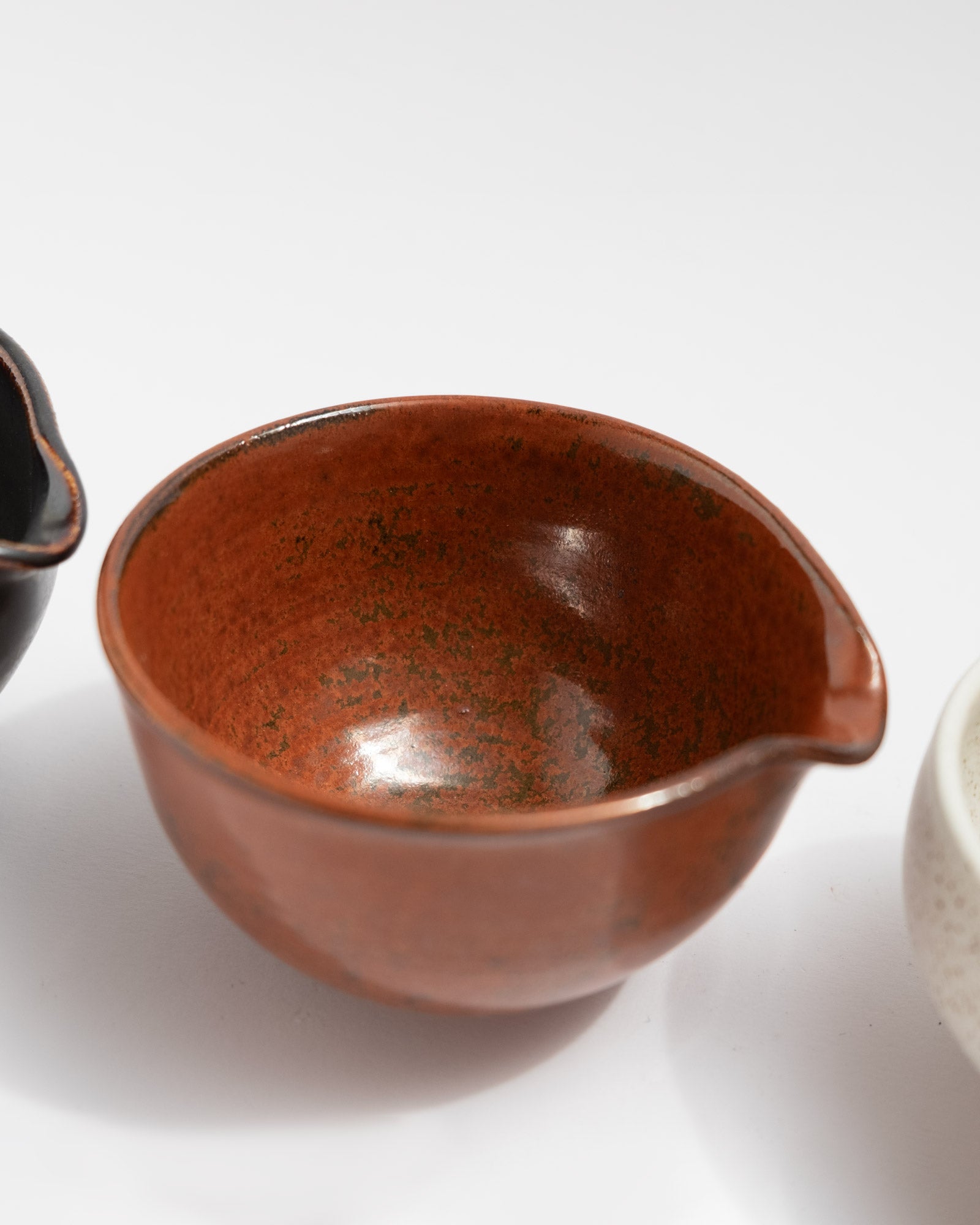 Handmade trio pouring set of small wheel-thrown stoneware bowls with black, rust-red, and speckled white glazes. Nesting design with functional spouts