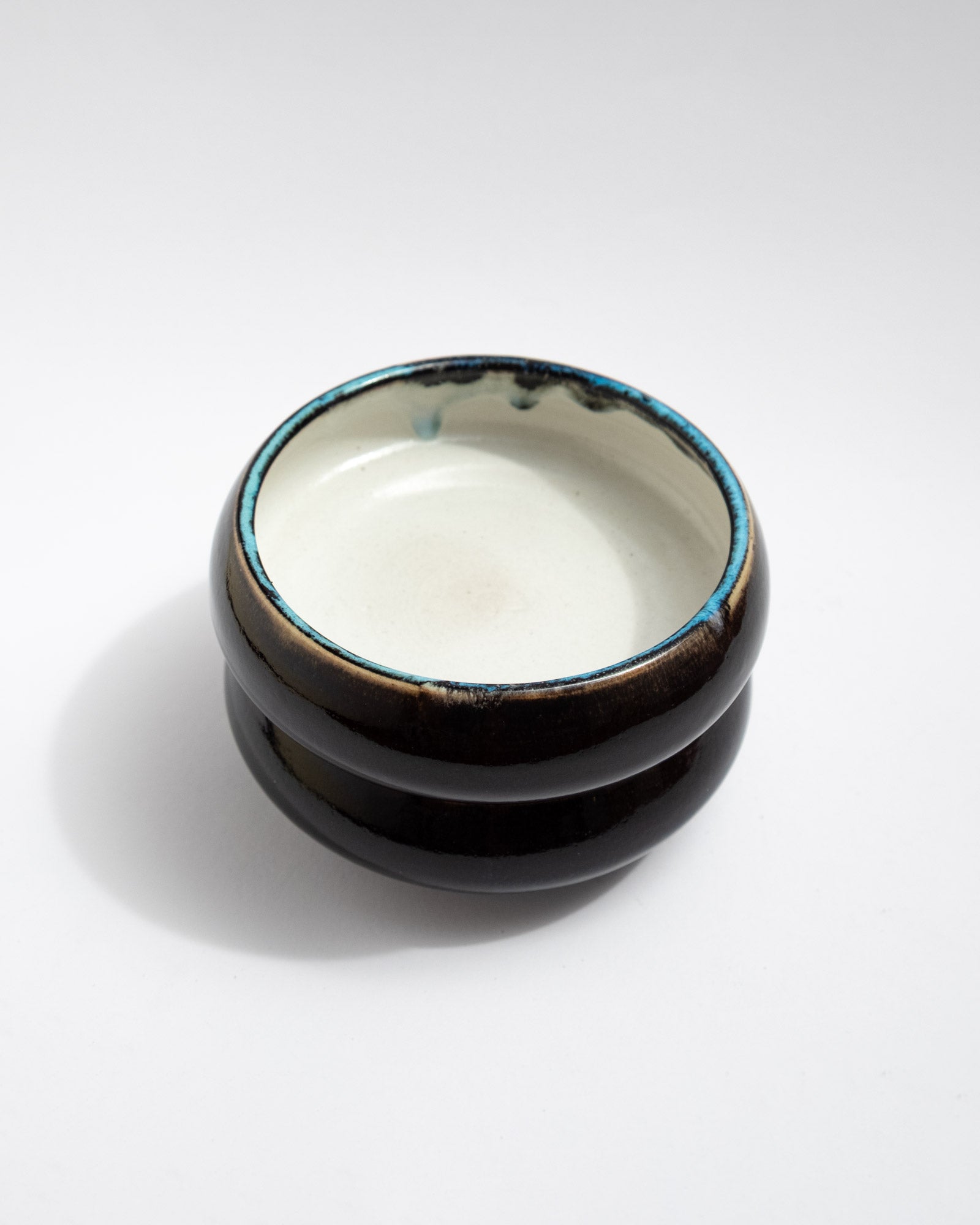 Small handmade bowl with white interior, dark exterior, and turquoise-rim detail