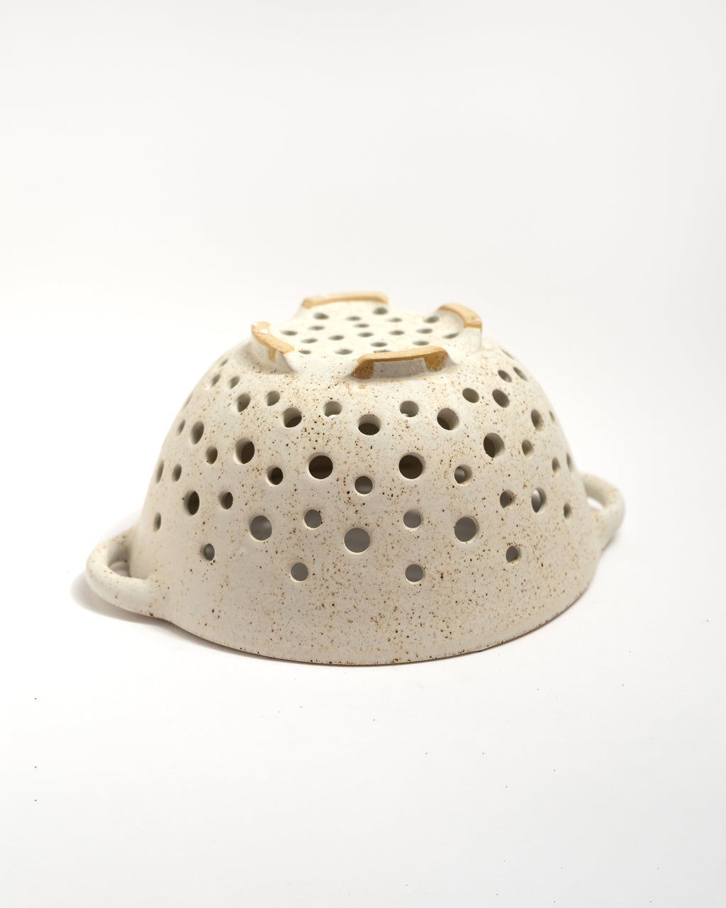 Speckled ceramic colander with a wooden handle on a white background