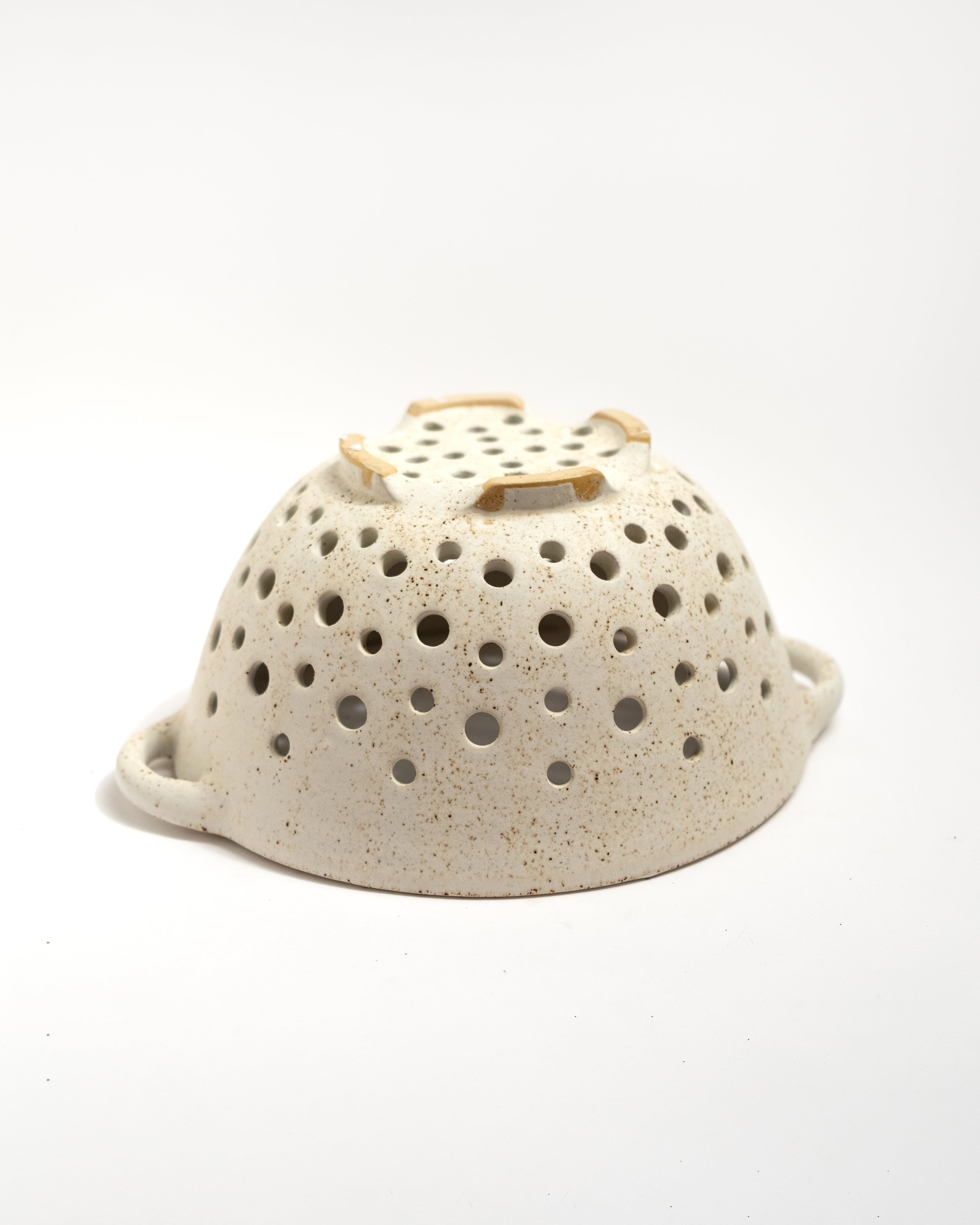Speckled ceramic colander with a wooden handle on a white background