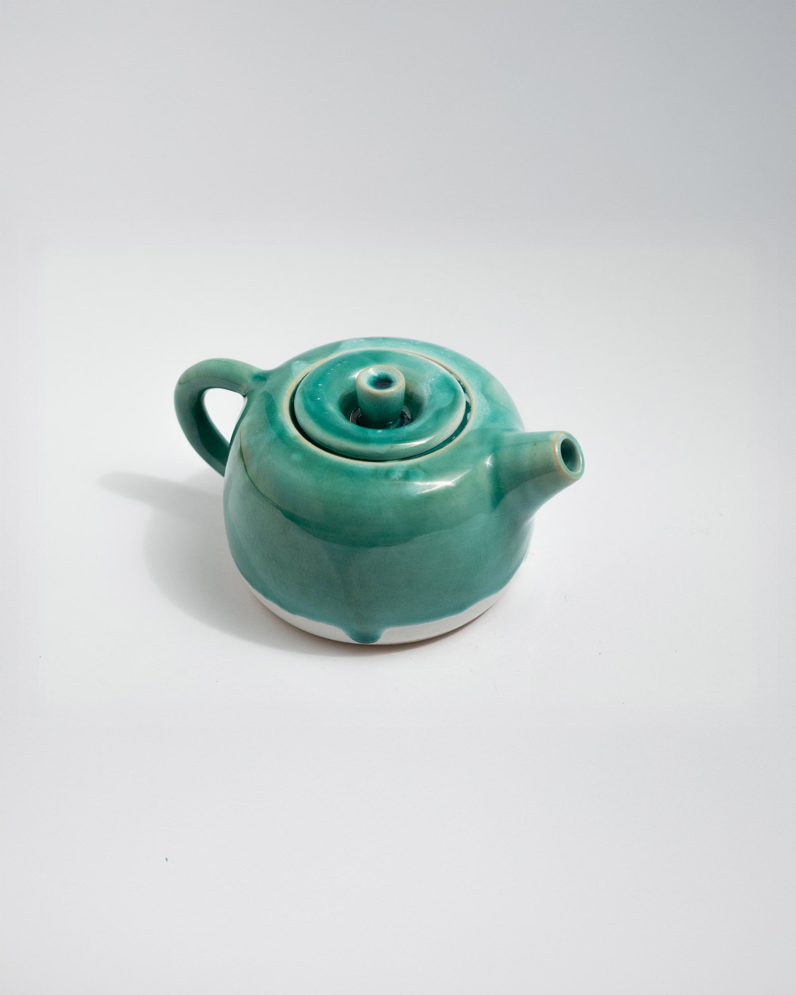 Teal ceramic teapot on a white background, handmade in Italy