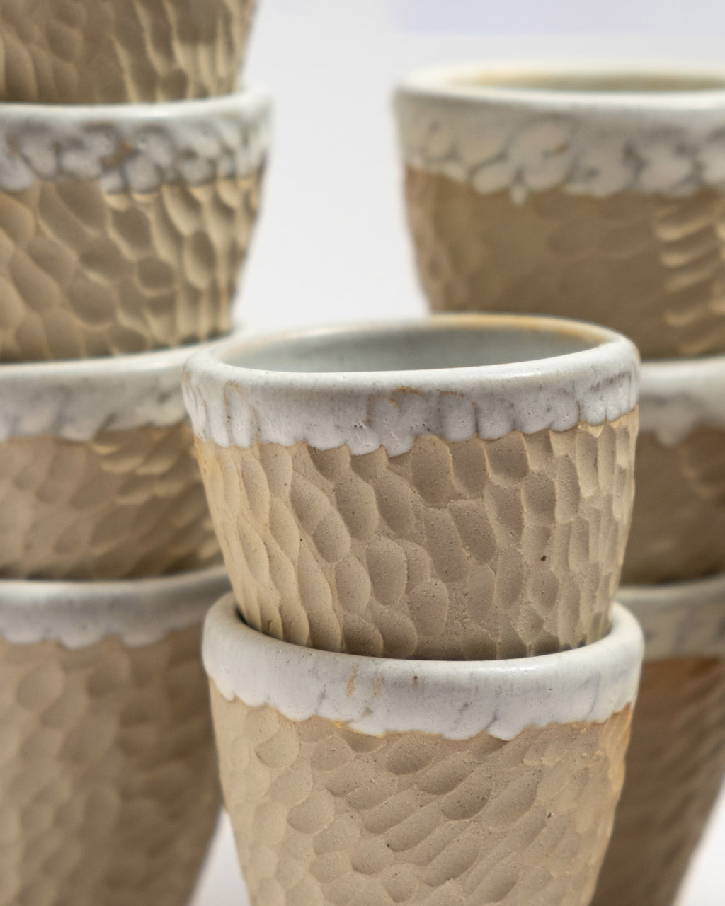 Closeup of textured ceramic cups with white rimmed edges on a light background