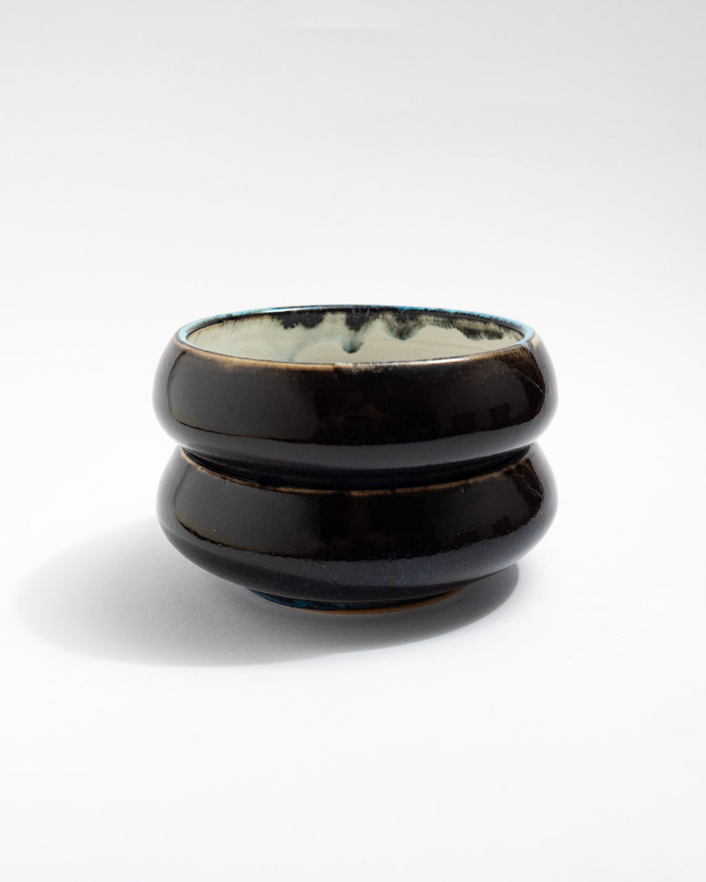 A small wheel-thrown bowl with a smooth white interior and a deep, glossy dark exterior