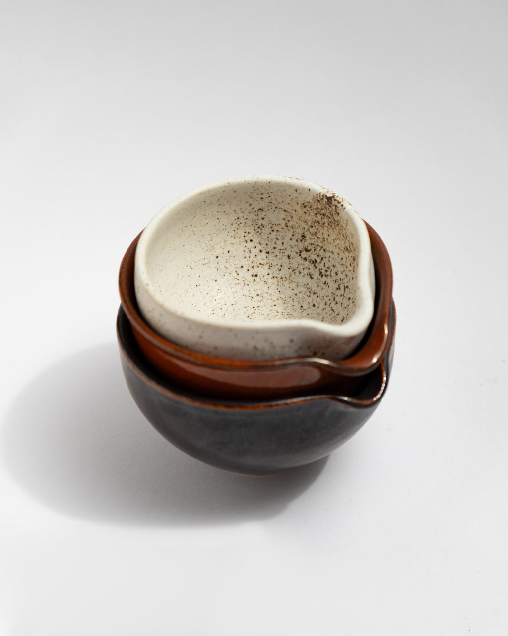 Set of three small handmade stoneware pouring bowls in black, rust-red, and speckled white glazes