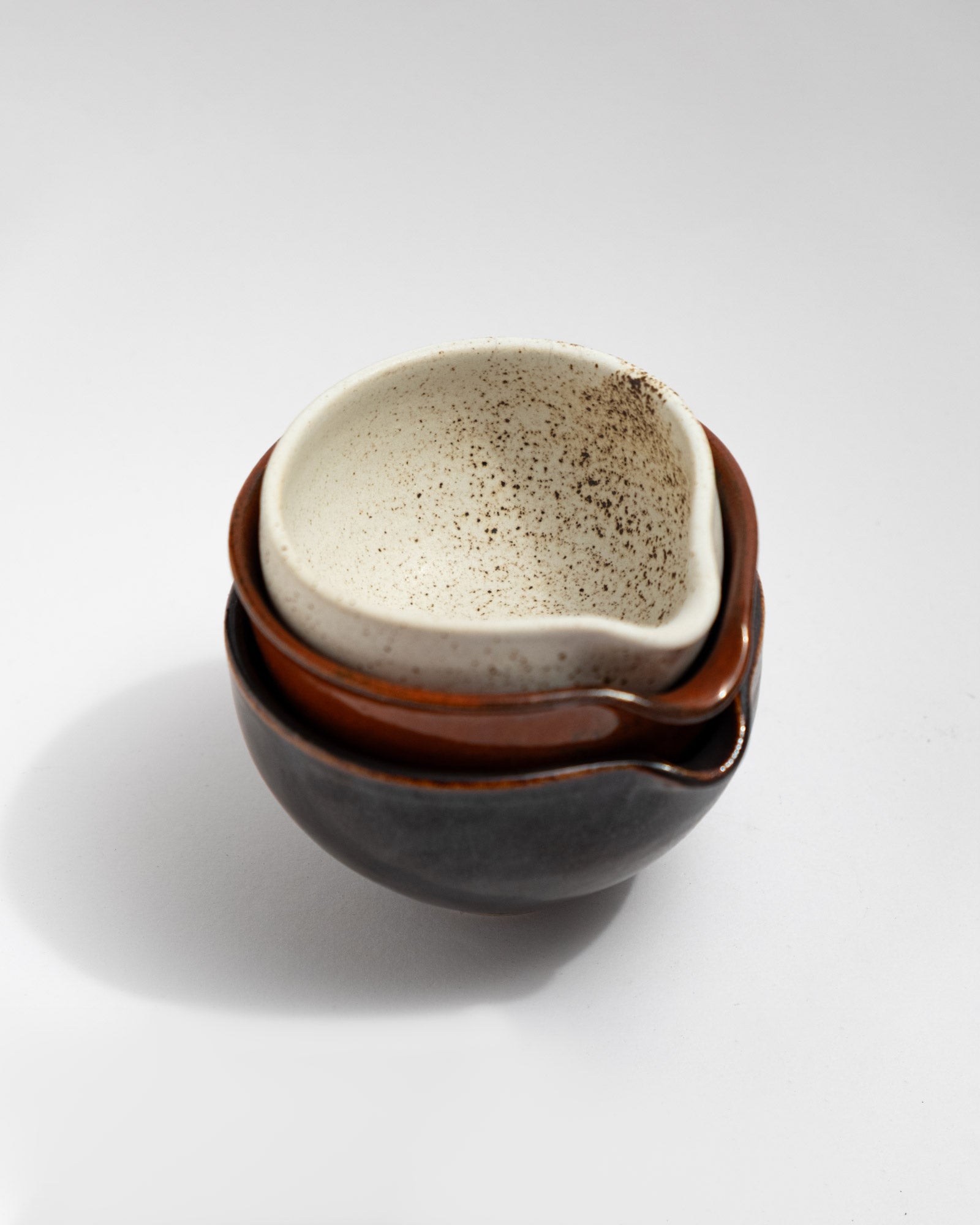Set of three small handmade stoneware pouring bowls in black, rust-red, and speckled white glazes