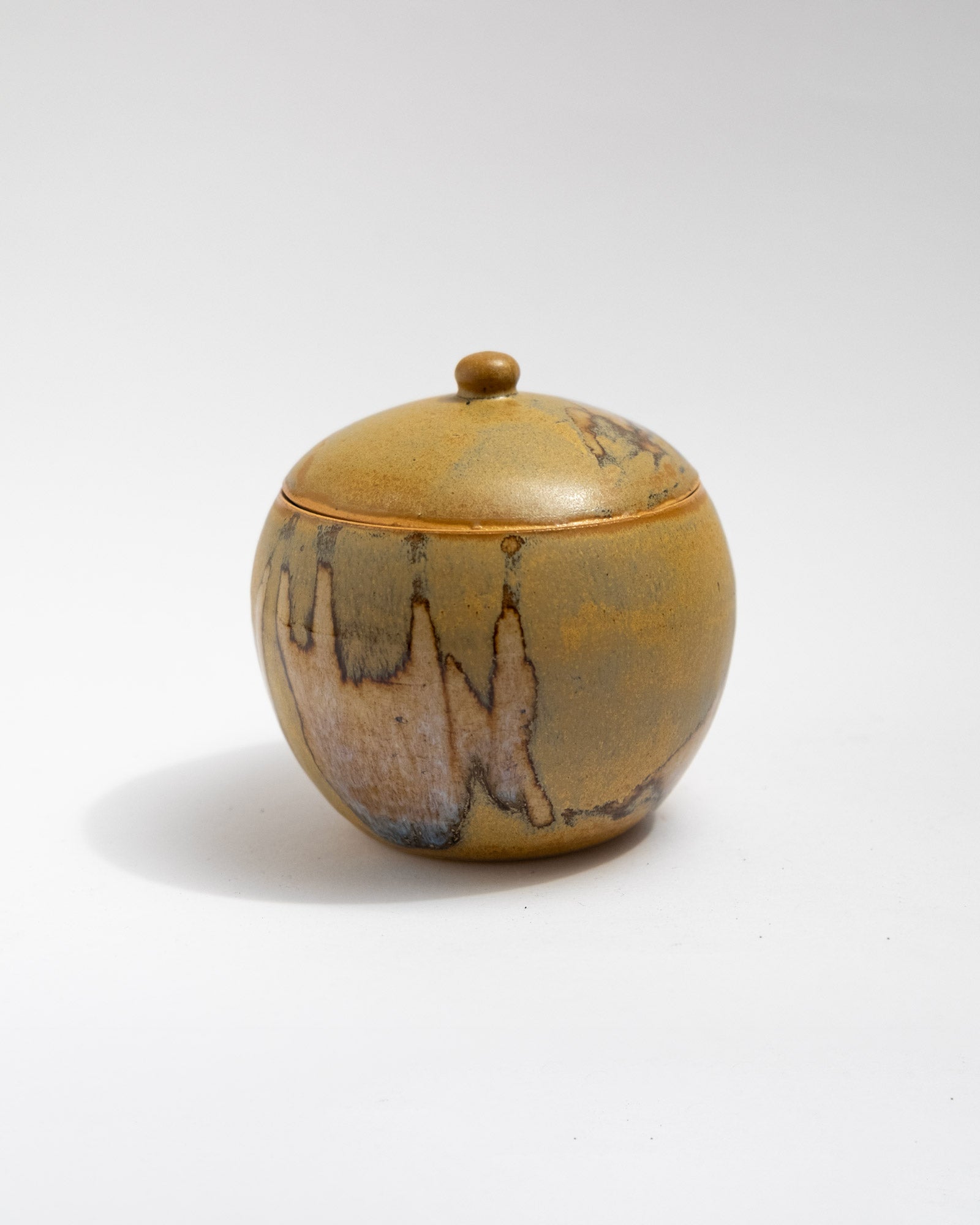 Handmade wheel-thrown stoneware lidded jar with warm ochre glaze and organic firing patterns. Artisan ceramic