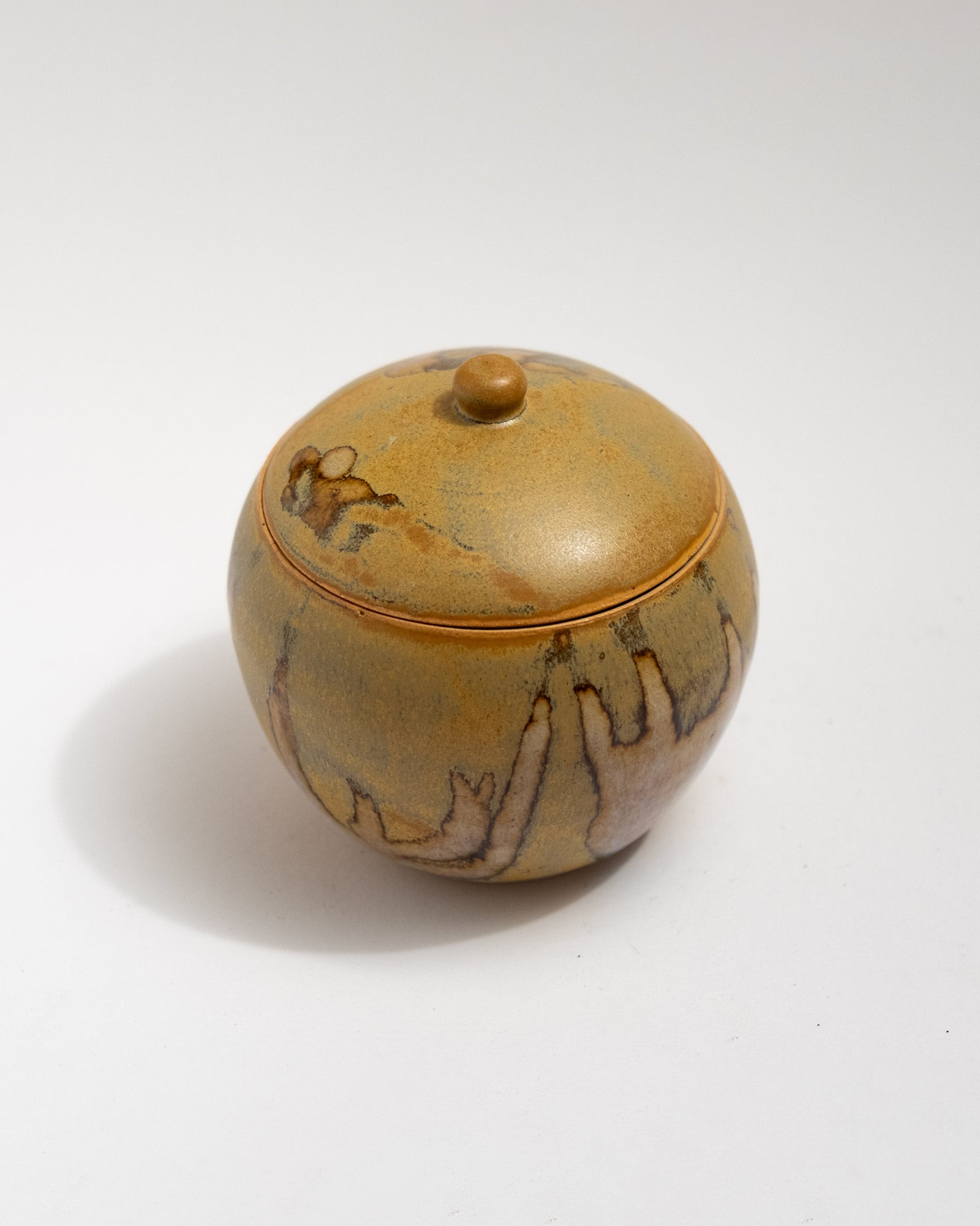 Handmade wheel-thrown stoneware lidded jar with warm ochre glaze and organic firing patterns. Artisan ceramic