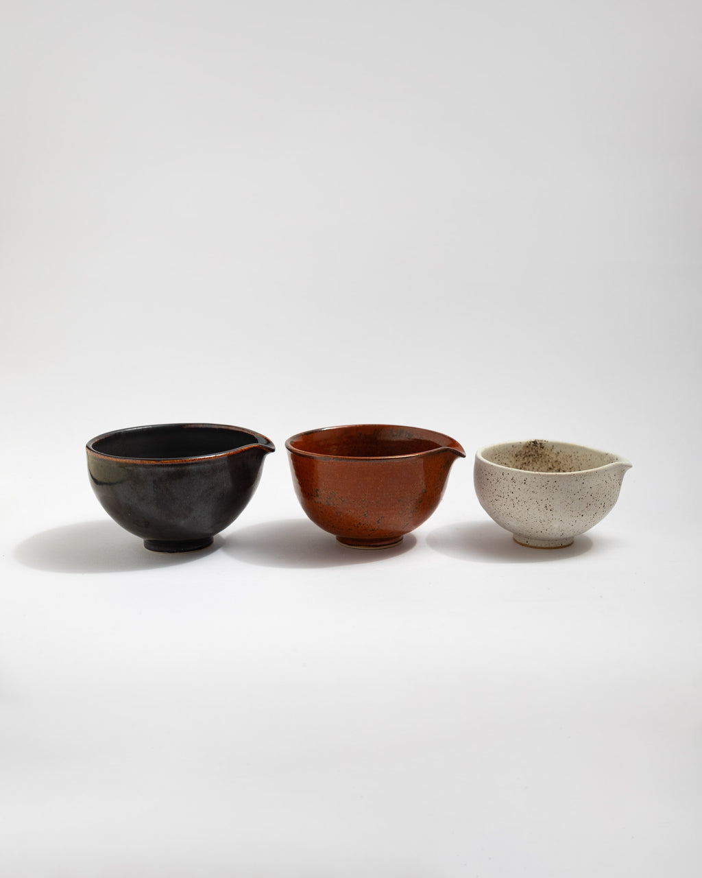 Set of three small handmade in Italy stoneware pouring bowls in black, rust-red, and speckled white glazes