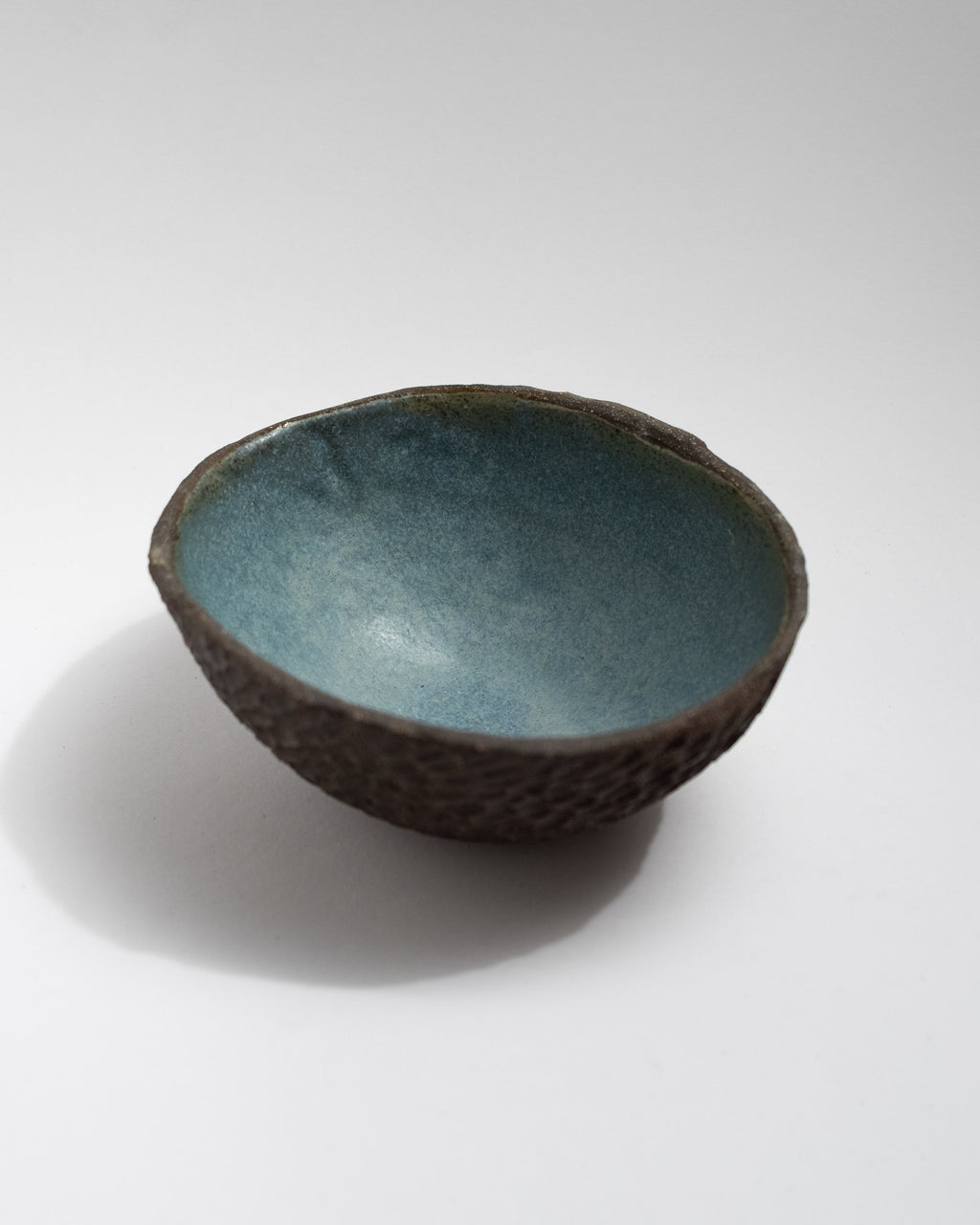 Hand-textured black clay bowl with scale-like surface and blue glazed interior